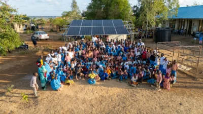 Un numeroso grupo de niños y adultos posa juntos al aire libre cerca de unos paneles solares en un día soleado.