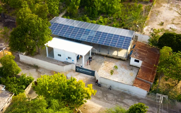 Vista aérea de un edificio blanco con paneles solares en el techo, rodeado de árboles y caminos de tierra.