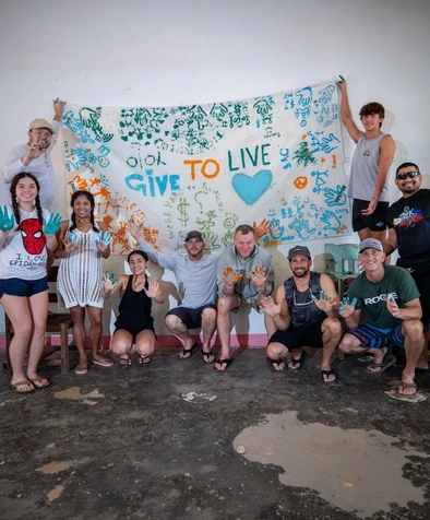Group posing in front of a decorated Give to Live banner, showing their paint-covered hands and smiling.