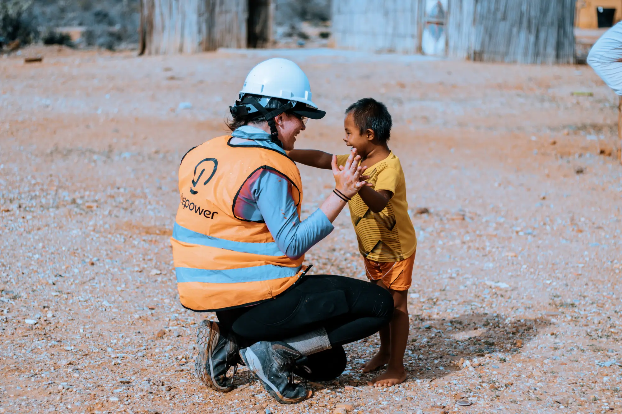 Un trabajador con chaleco de seguridad y casco sonríe mientras juega con un niño pequeño al aire libre.