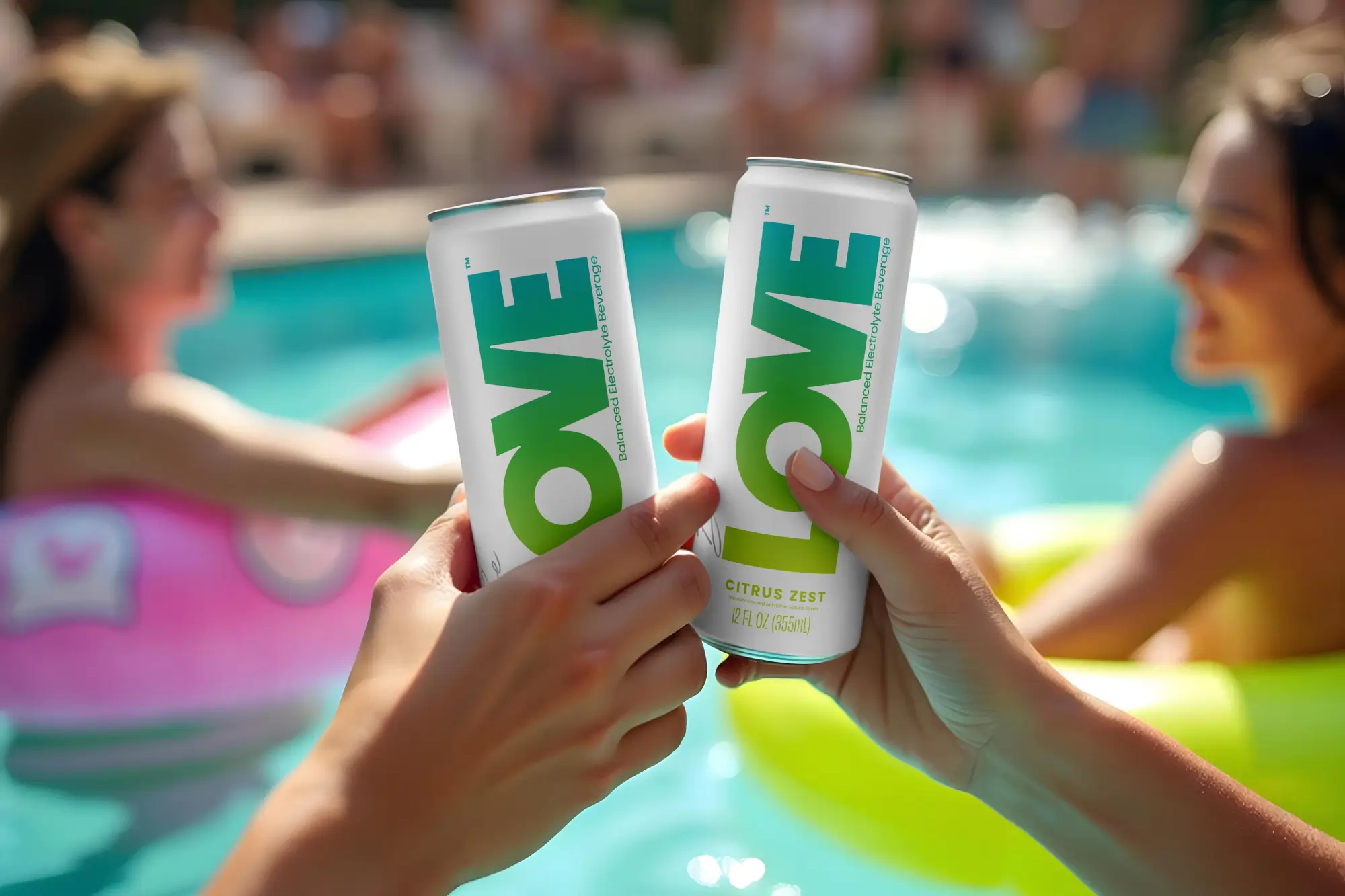 Dos manos sostienen latas de LOVE Citrus Zest junto a una alberca, con personas relajándose en flotadores al fondo.