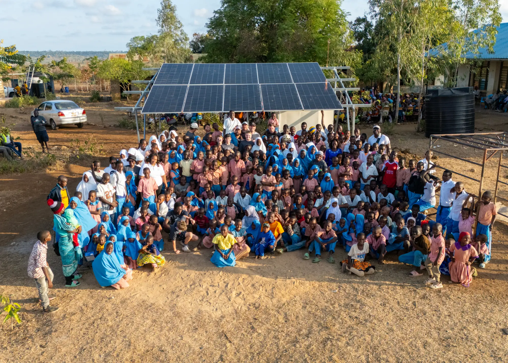 Un grupo numeroso de personas posa al aire libre frente a unos paneles solares en un día soleado.