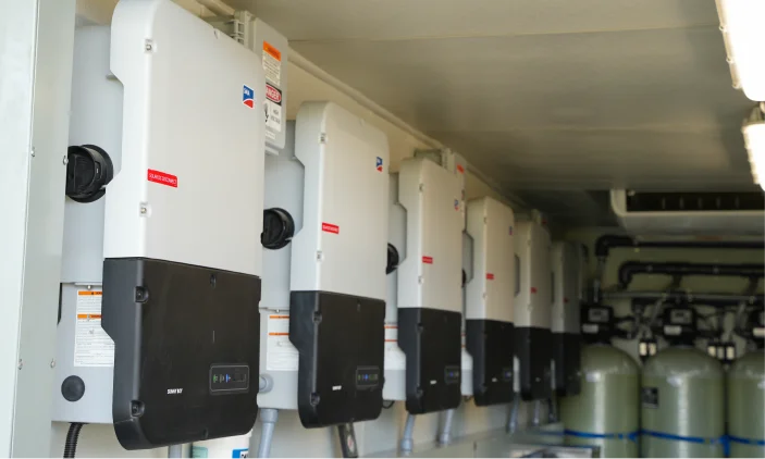 A row of wall-mounted solar inverters inside a container