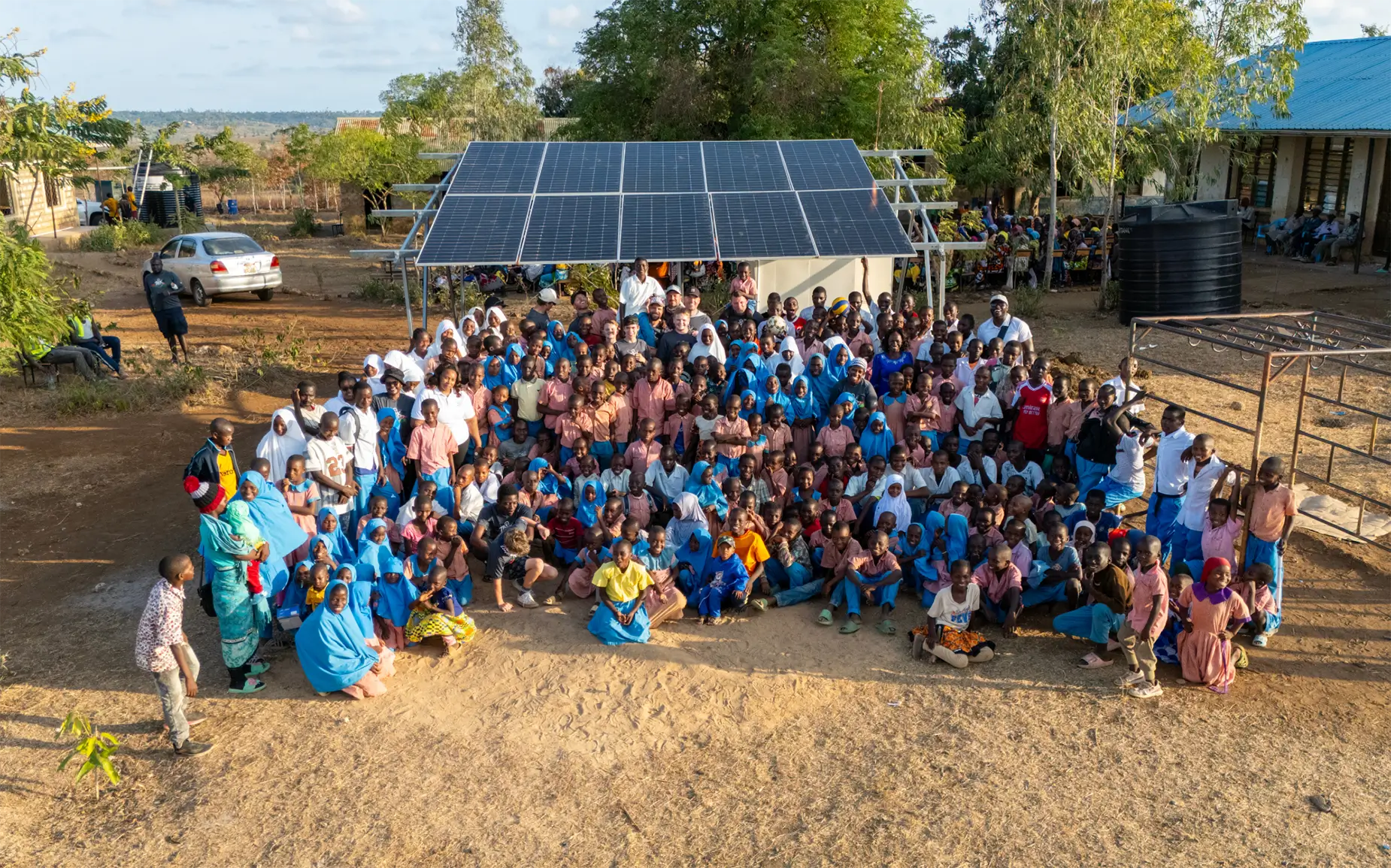 Un grupo numeroso posa junto a unos paneles solares, mostrando cómo la energía solar beneficia a las comunidades remotas en un entorno rural y soleado.