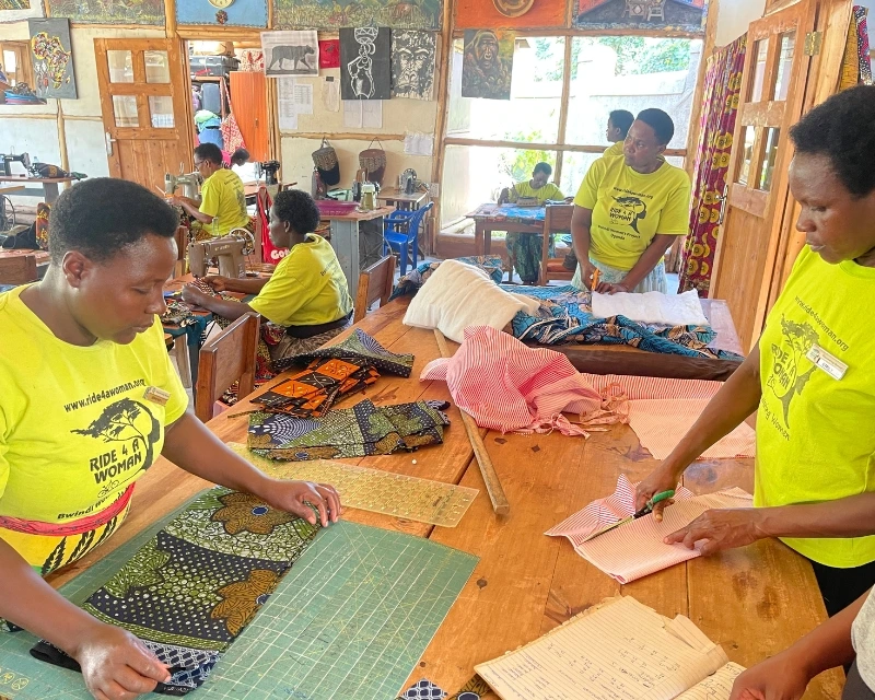 Women in yellow shirts cutting and arranging fabric pieces on tables in a bright sewing workshop.