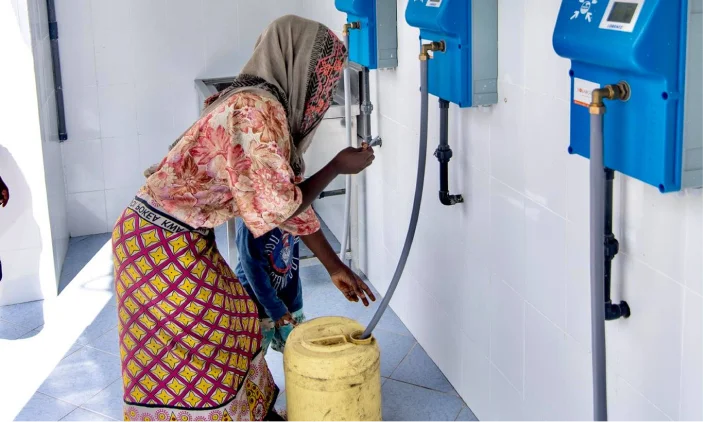 A woman filling a jerrycan at a blue automatic water dispenser