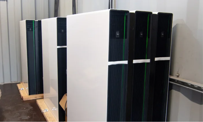 Four white and black server cabinets are lined up inside a room with grey metal walls.