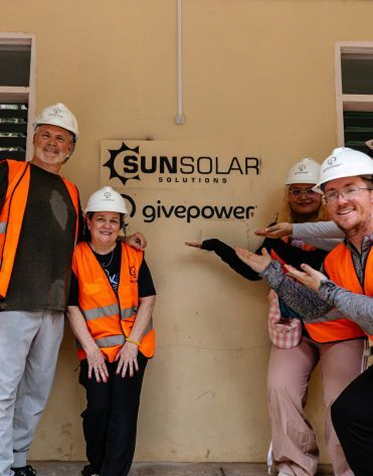 Four people in hard hats and hi-vis vests beside a SunSolar Solutions and GivePower sign