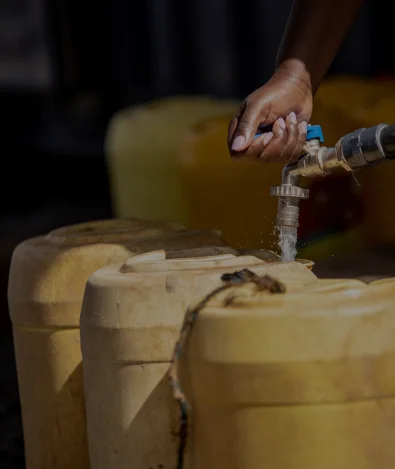 A hand fills a yellow plastic container with water from a tap.