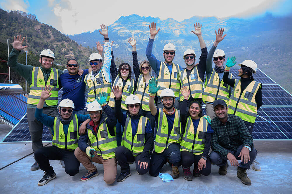 GivePower team in hard hats and hi-vis vests beside a solar array in the mountains