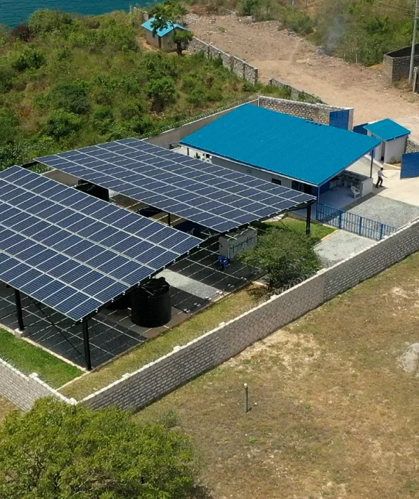 Aerial view of a solar panel array beside a blue-roofed building, surrounded by a stone wall.